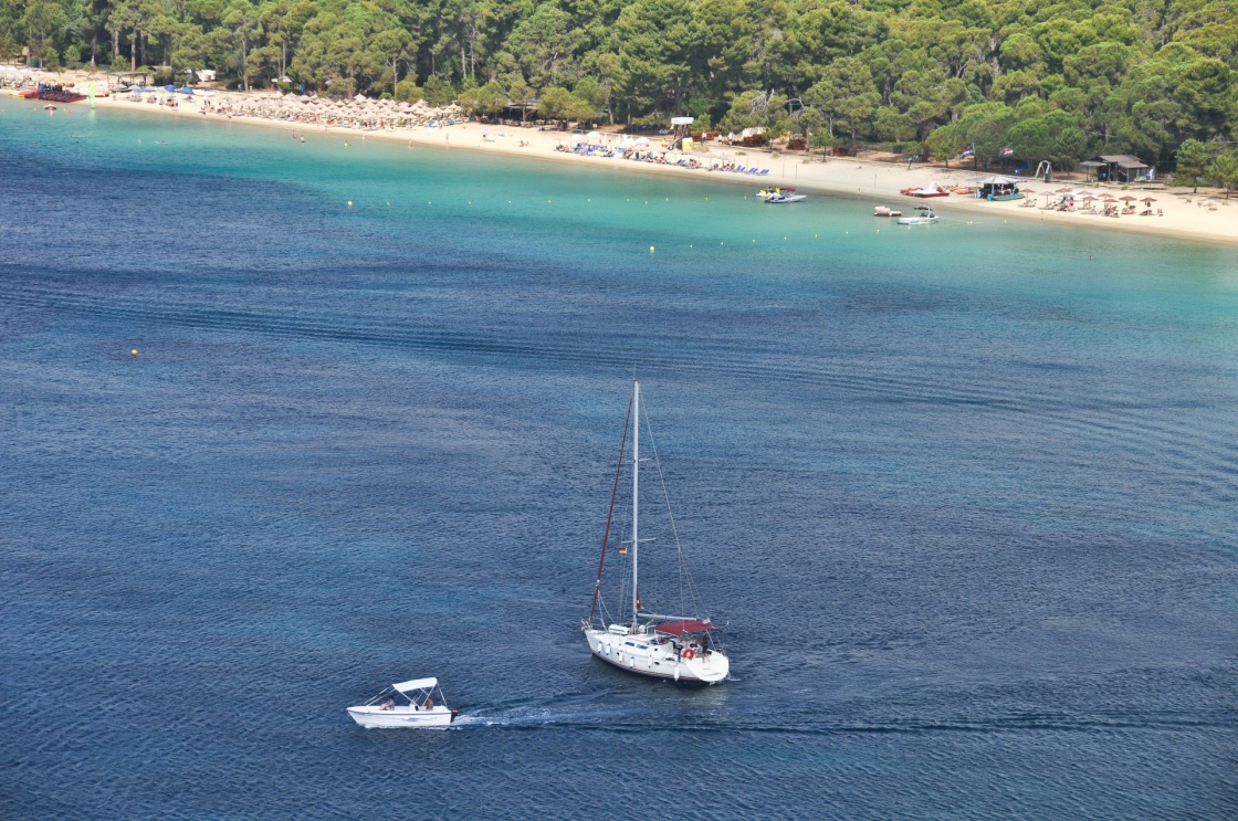 Kanapitsa Beach with sunbathers, sailboats and speedboats in a deep blue Aegean sea.